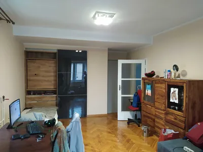 Przestronny, umeblowany pokój z drewnianą podłogą, dużą szafą przesuwną, komodą, biurkiem z monitorem, łóżkiem oraz jasnymi ścianami w mieszkaniu do wynajęcia.